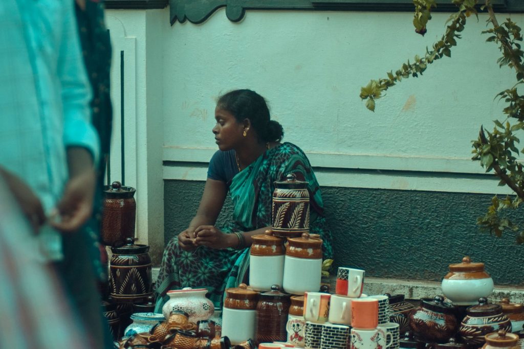 A woman beside her pottery stall at an outdoor market in India