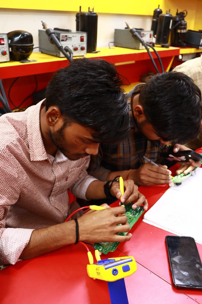 Young trainees learning circuit-board repair in an electronics workshop